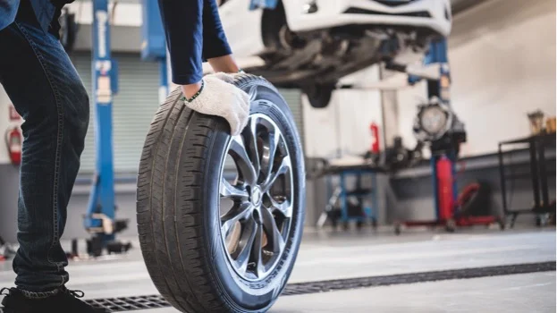 Mécanicien en gants blancs manipulant un pneu de voiture près d'un véhicule levé à Virazeil près de Marmande dans le Lot-et-Garonne 47